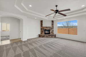 Unfurnished living room featuring light colored carpet, arched walkways, recessed lighting, a stone fireplace, and ceiling fan