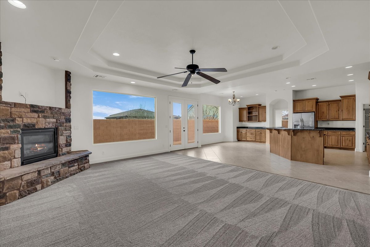 Unfurnished living room featuring light tile patterned floors, hanging lights, ceiling fan, a stone fireplace, and healthy amount of natural light