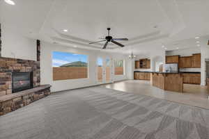 Unfurnished living room featuring light tile patterned floors, hanging lights, ceiling fan, a stone fireplace, and healthy amount of natural light