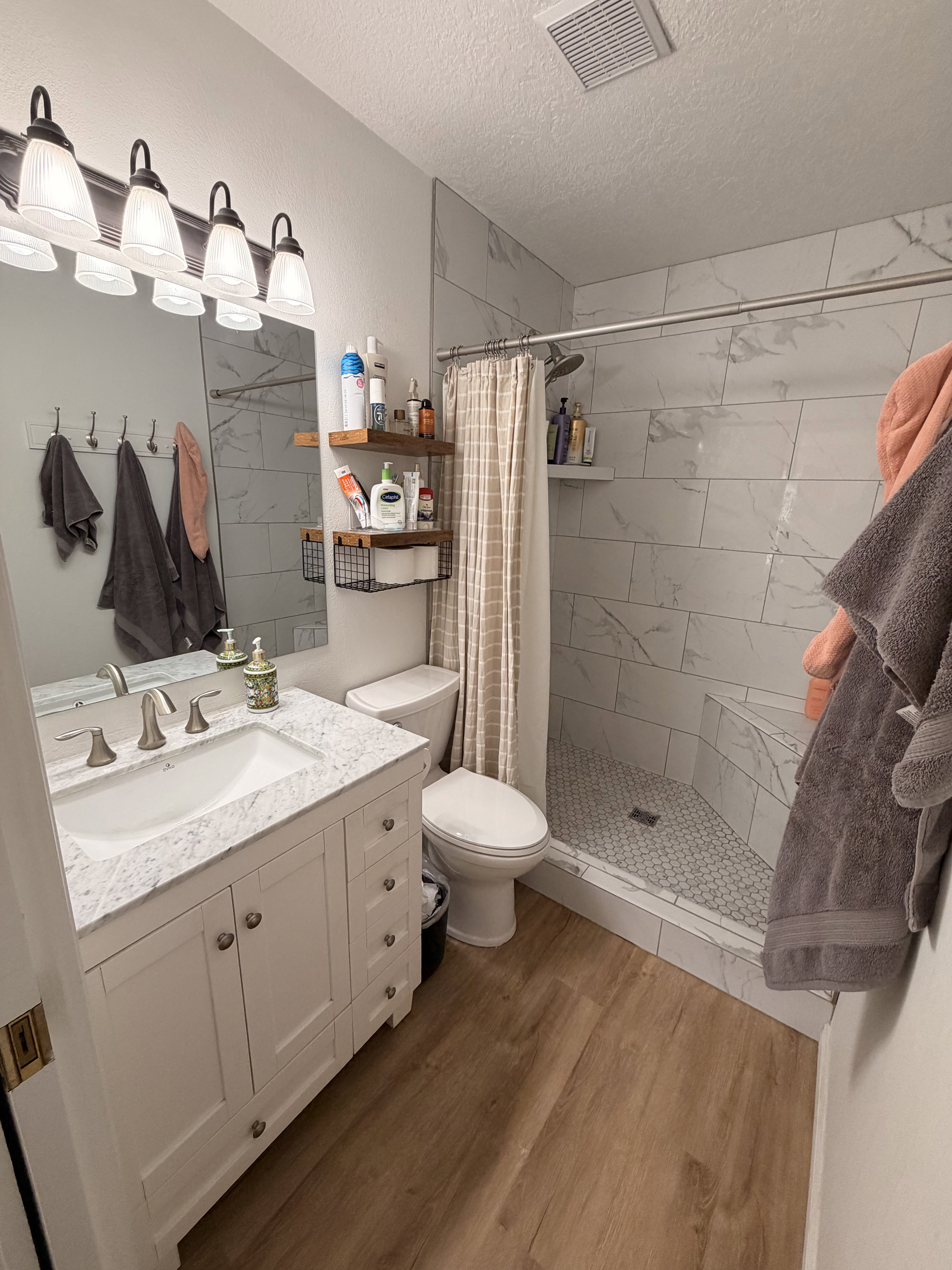Full bath with vanity, a shower stall, light wood-type flooring, and a textured ceiling