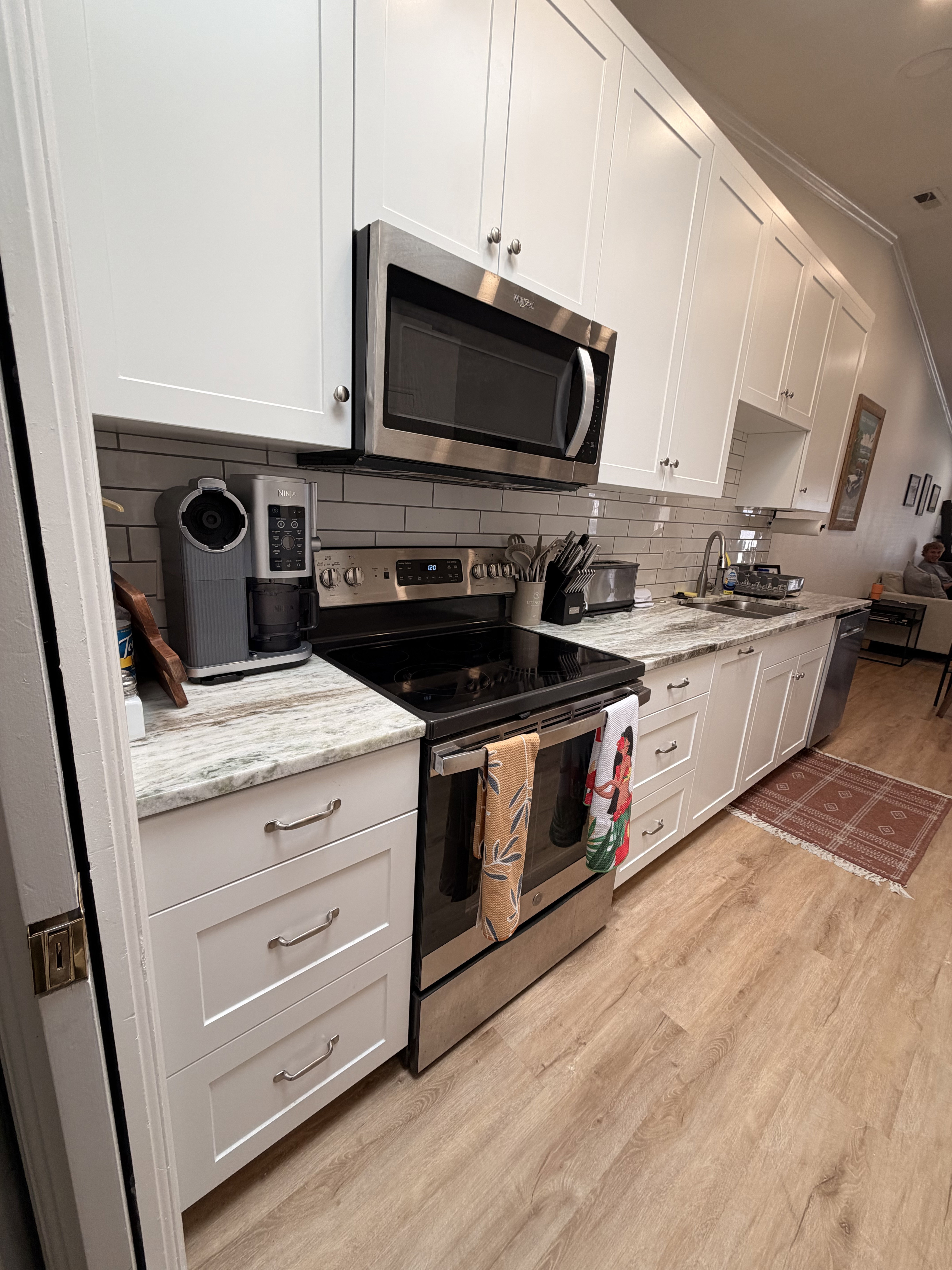 Kitchen with stainless steel appliances, ornamental molding, white cabinetry, light wood-style floors, and light stone countertops