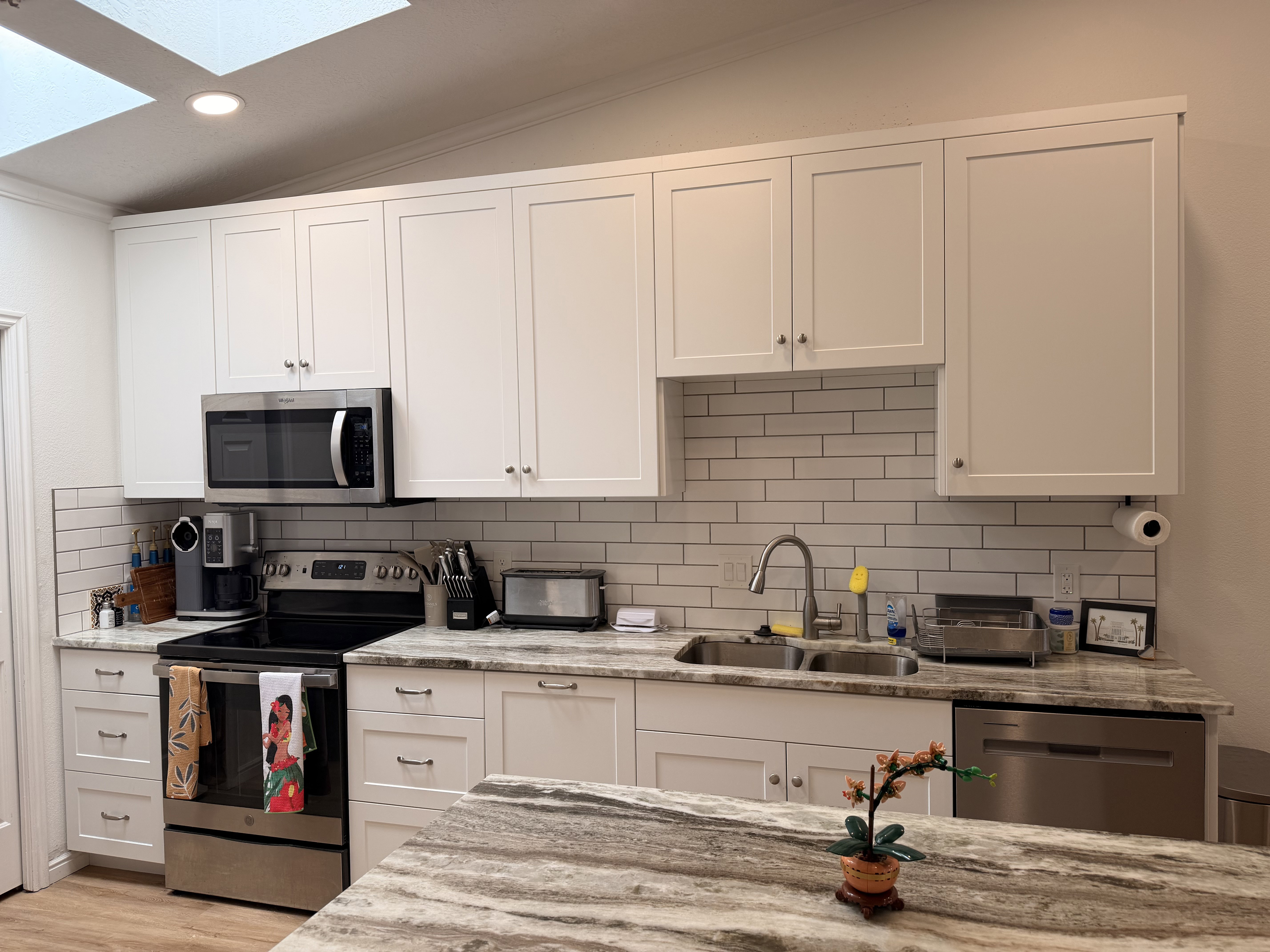 Kitchen featuring stainless steel appliances, white cabinets, light stone counters, lofted ceiling, and recessed lighting