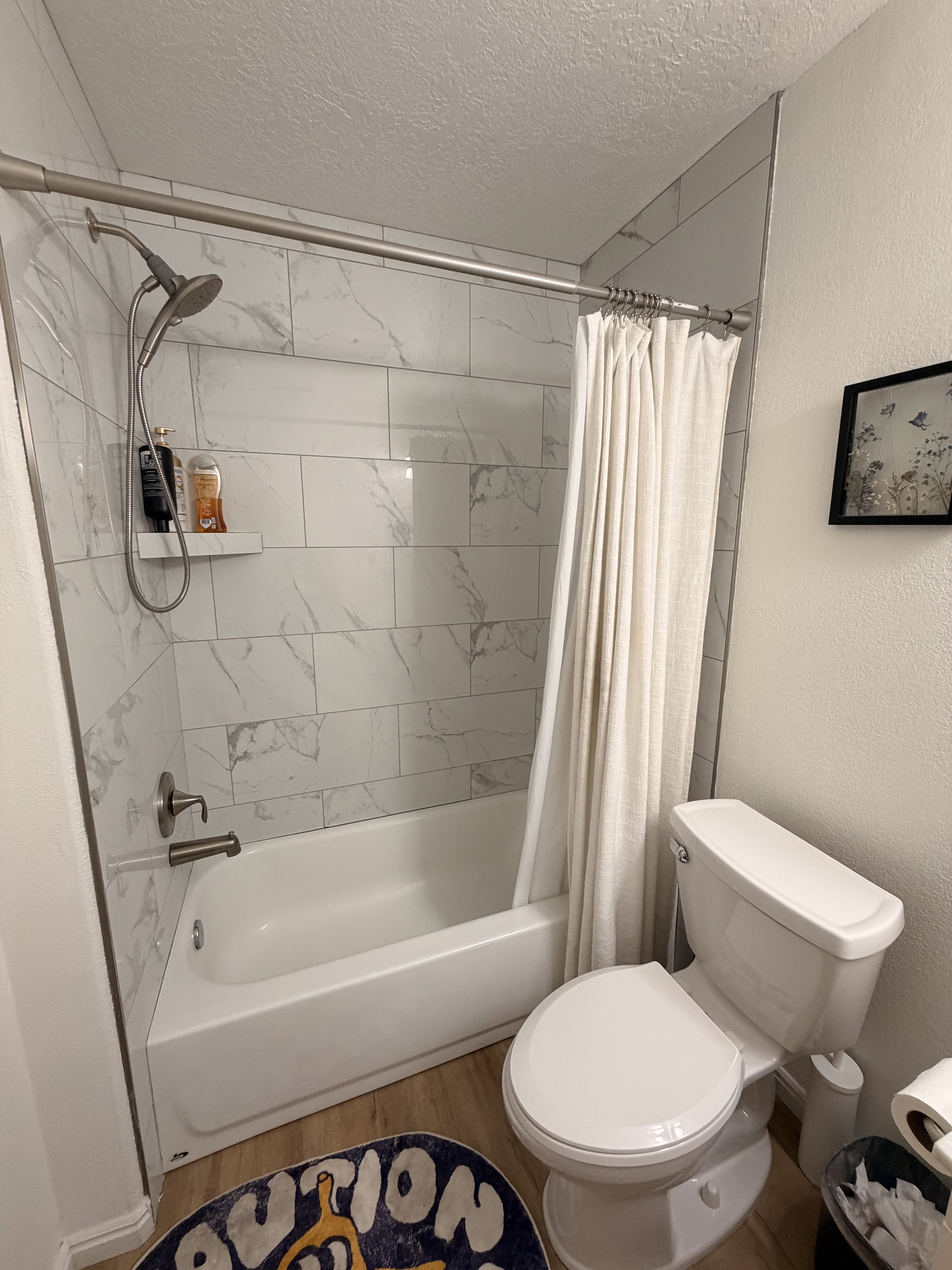 Full bath with a textured wall, a textured ceiling, wood finished floors, and shower / bath combo