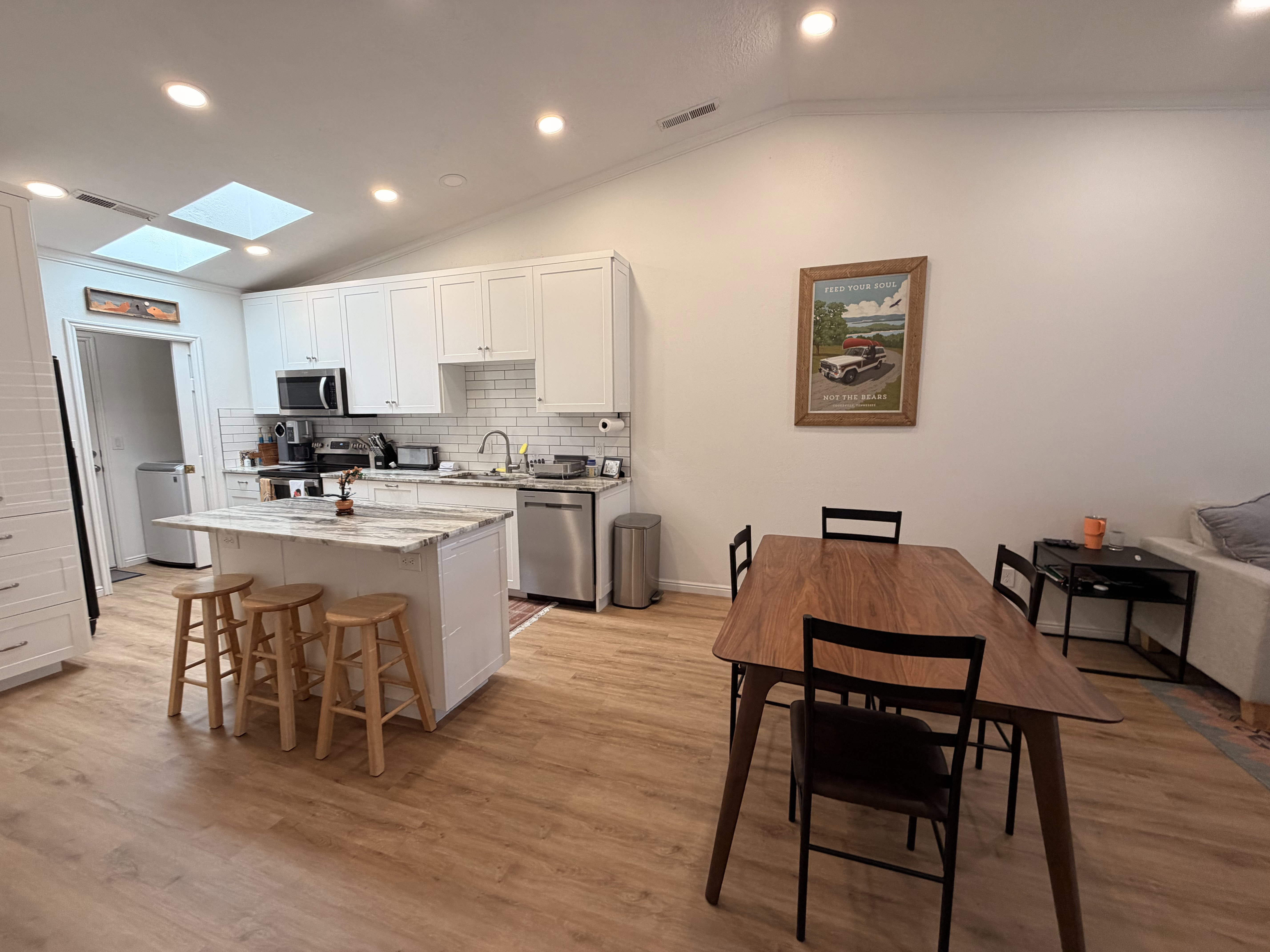 Kitchen with lofted ceiling, white cabinets, recessed lighting, light stone counters, and a kitchen breakfast bar