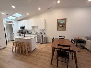 Kitchen with lofted ceiling, white cabinets, recessed lighting, light stone counters, and a kitchen breakfast bar