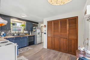 Kitchen with white electric stove, blue cabinets, dishwasher, light wood finished floors, and tasteful backsplash