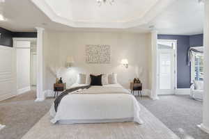 Primary Suite Carpeted bedroom featuring decorative columns, a raised ceiling, and access to exterior