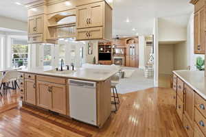 Kitchen featuring open floor plan, light wood-style floors, dishwasher, a kitchen breakfast bar, and light wood finish cabinetry