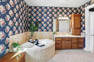 Primary Suite Full bath featuring vanity, a garden tub, wallpapered walls, and light carpet
