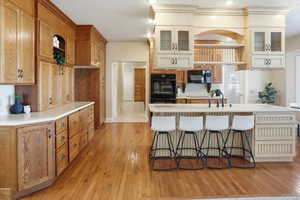 Kitchen with a kitchen breakfast bar, light countertops, light wood-style floors, and glass insert cabinets