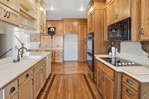 Kitchen with light countertops, black appliances, light wood-type flooring, recessed lighting, and glass insert cabinets