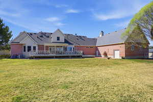 Rear view of property with brick siding, a deck, a lawn, and a shingled roof