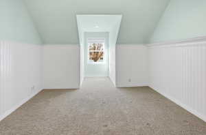 Bedroom with wainscoting, vaulted ceiling, wood walls, and carpet floors