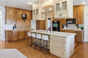 Dual tone kitchen with dual tone cabinets, light countertops, light wood finished floors, a breakfast bar area, and glass insert cabinets