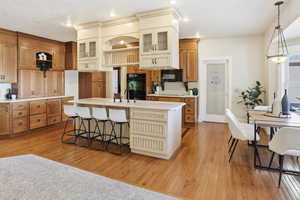 Kitchen with light wood finished floors, a kitchen breakfast bar, light countertops, glass insert cabinets, and two tone color scheme