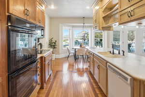 Kitchen featuring black appliances, light wood finished floors, light countertops, an island with sink, and pendant lighting