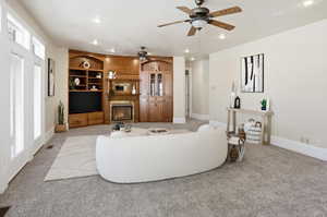 Living room featuring a ceiling fan, recessed lighting, a glass covered fireplace, and light carpet