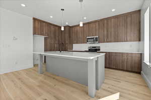 Kitchen with a center island with sink, light wood-style floors, stainless steel appliances, hanging light fixtures, and light stone counters