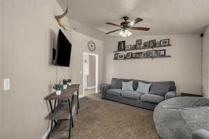 Carpeted living room featuring ceiling fan and baseboards