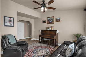 Living area with arched walkways, ceiling fan, light carpet, and vaulted ceiling