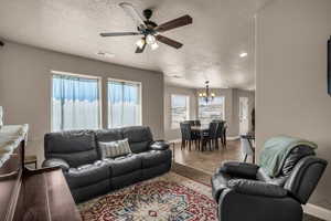 Living room featuring a ceiling fan, a textured ceiling, a chandelier, and light tile patterned floors