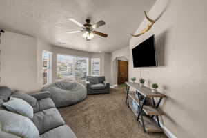 Living area featuring a ceiling fan, a textured ceiling, and carpet flooring