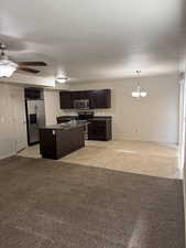Kitchen with dark wood finish cabinets, light colored carpet, ceiling fan, stainless steel appliances, and a center island with sink