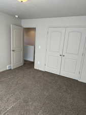 Unfurnished bedroom with dark colored carpet, a closet, and a textured ceiling