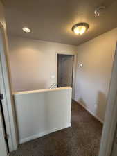 Corridor featuring an upstairs landing, dark carpet, and a textured ceiling