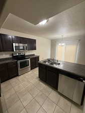 Kitchen featuring stainless steel appliances, dark wood finish cabinetry, a textured ceiling, hanging lights, and dark countertops