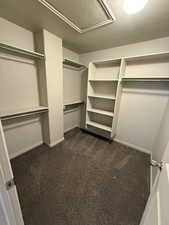 Walk in closet with dark colored carpet and attic access