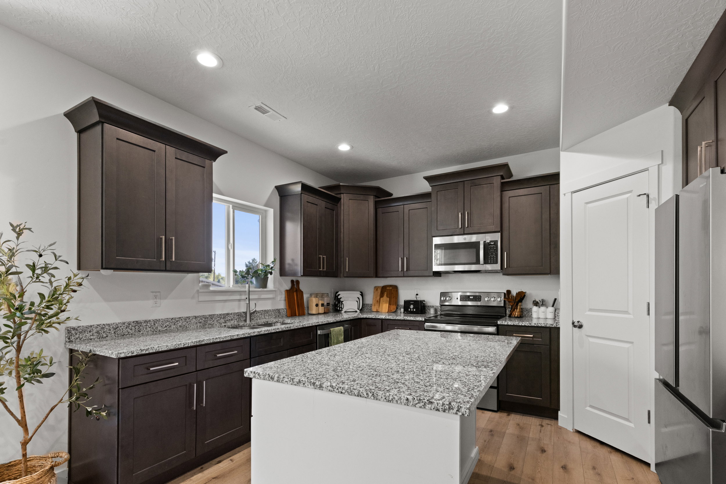Kitchen with dark wood finish cabinets, stainless steel appliances, light stone countertops, light wood-style flooring, and recessed lighting
