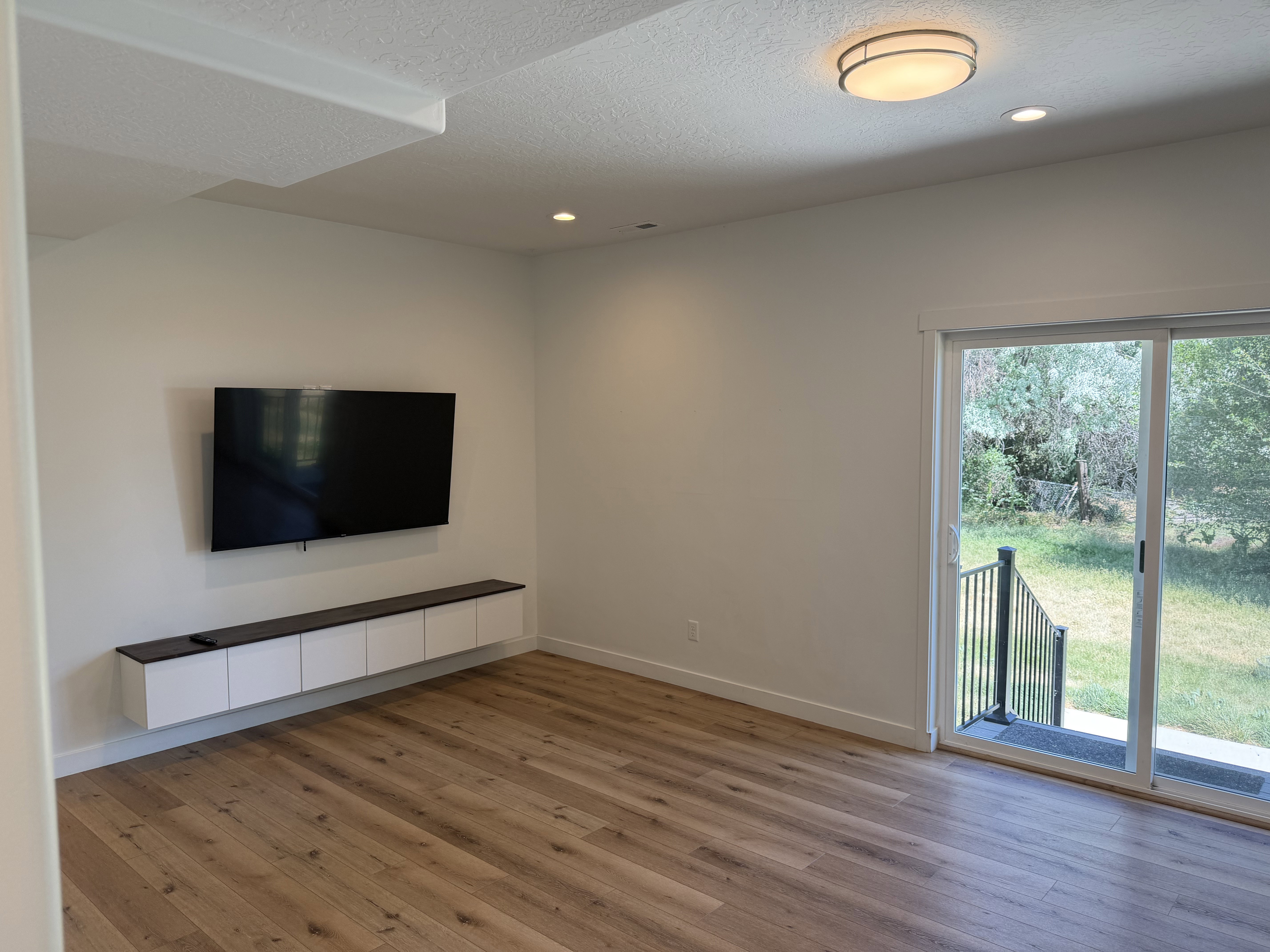 Spacious room featuring wood-finish flooring, a built-in floating entertainment console, and recessed ceiling lighting