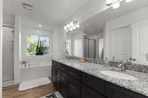 Full bathroom featuring a stall shower, double vanity, light wood-style flooring, and a garden tub