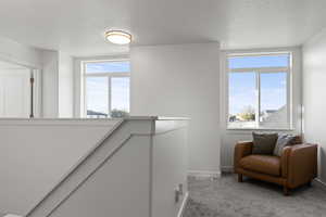 Living area featuring light carpet, a textured ceiling, and an upstairs landing