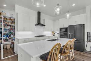Kitchen with black appliances, white cabinetry, dark wood finished floors, a center island with sink, and decorative light fixtures