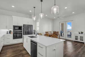 Kitchen with black appliances, a center island with sink, white cabinetry, and light stone counters