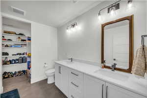 Full bath with double vanity, a walk in closet, and concrete floors