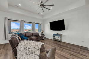 Living area with ceiling fan, wood finished floors, a raised ceiling, and recessed lighting
