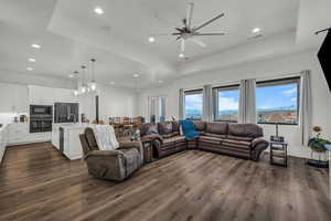 Living room featuring a ceiling fan, a tray ceiling, dark wood-style floors, healthy amount of natural light, and recessed lighting