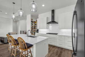 Kitchen featuring a kitchen bar, fridge, white cabinets, a center island with sink, and dark wood-type flooring