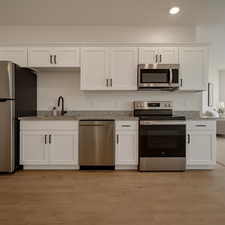 Kitchen featuring white cabinets, stainless steel appliances, light stone countertops, light wood-type flooring, and recessed lighting