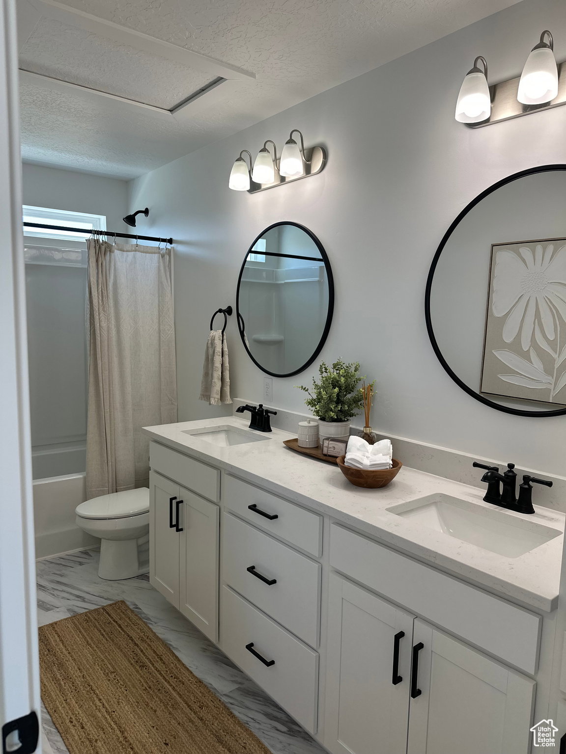Bathroom featuring double vanity, a textured ceiling, shower / tub combo, and light marble finish flooring