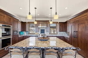 Kitchen featuring a kitchen breakfast bar, stainless steel appliances, light stone countertops, and hanging light fixtures