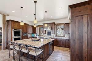 Kitchen with an island with sink, light stone counters, a kitchen breakfast bar, decorative light fixtures, and stainless steel appliances