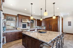 Kitchen featuring tasteful backsplash, light stone countertops, an island with sink, a kitchen breakfast bar, and range hood