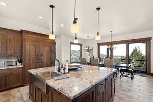 Kitchen with light stone countertops, a center island with sink, suspended lighting, a breakfast bar area, and dark wood finish cabinets