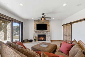 Living area featuring a barn door, a ceiling fan, light colored carpet, a fireplace, and recessed lighting