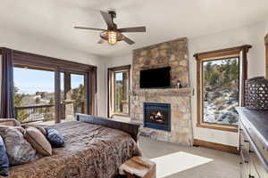 Bedroom featuring a stone fireplace, light colored carpet, and ceiling fan