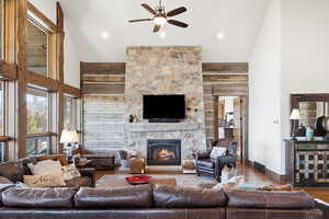 Living room with hardwood / wood-style floors, a ceiling fan, a stone fireplace, vaulted ceiling, and wooden walls